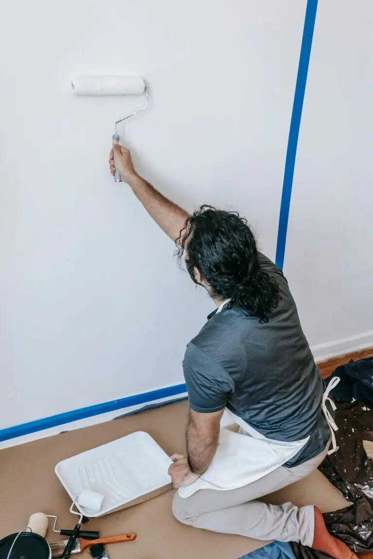 Professional painter rolling an interior wall with blue painters tape and a roller tray